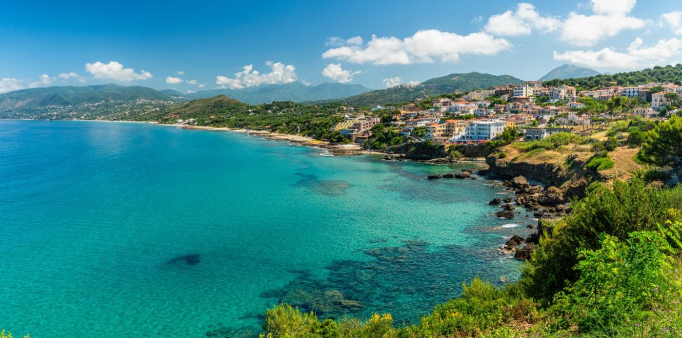 Panorama costiero con mare cristallino e pittoresco villaggio su colline verdi.