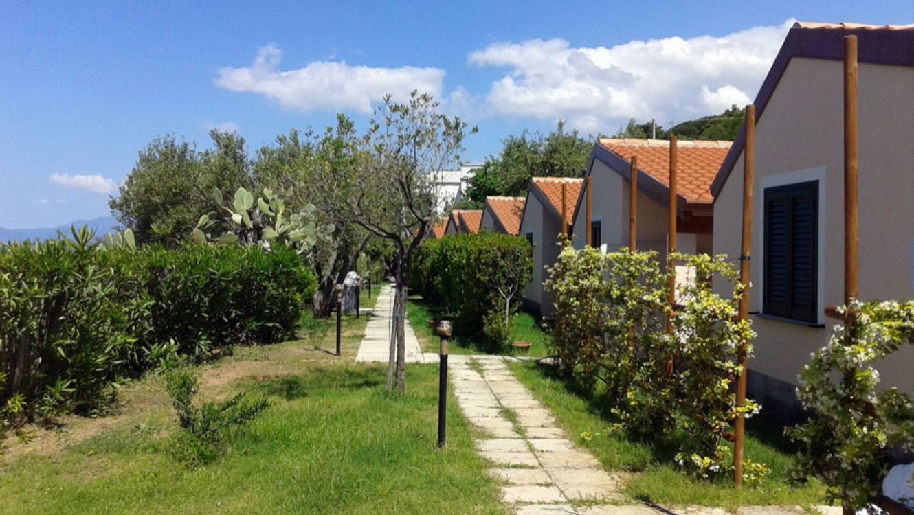 Villette a schiera con tetti rossi e giardino verde, sotto un cielo sereno.