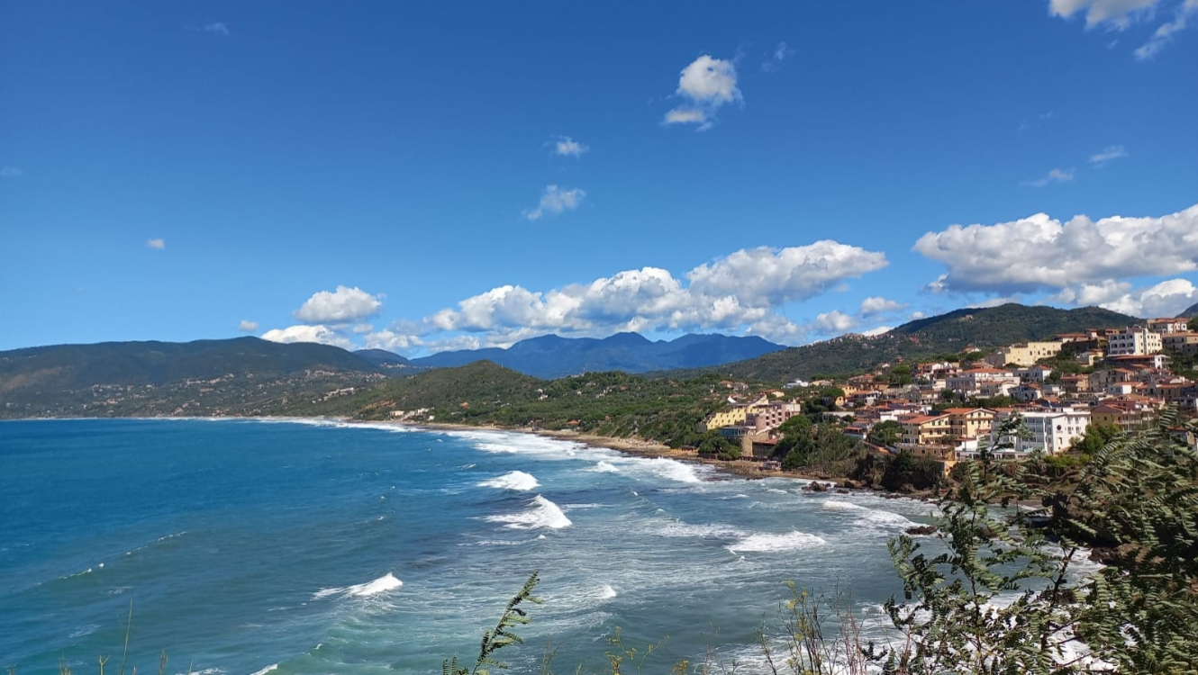 Vista costiera con mare blu, onde e un pittoresco villaggio collinare.