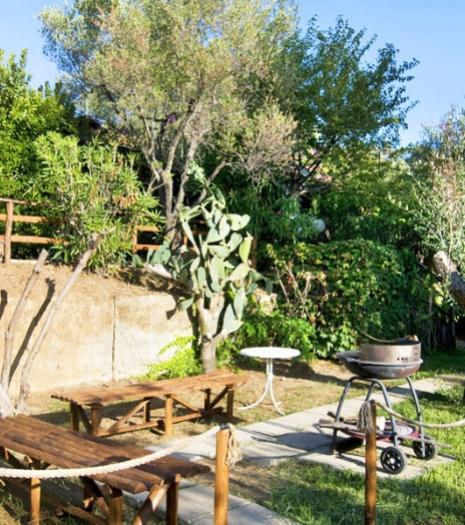 Giardino con tavoli in legno, barbecue e vegetazione rigogliosa.