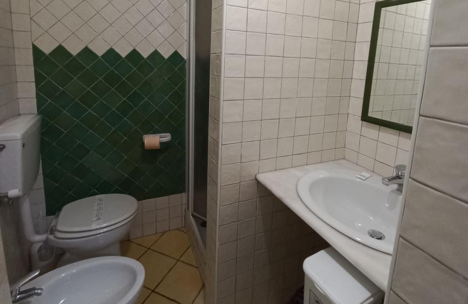 Bagno con piastrelle verdi e beige, doccia, lavabo, WC e bidet.