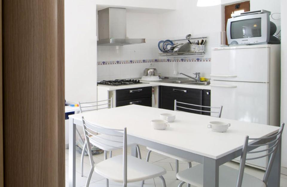 Cucina moderna con tavolo bianco, sedie in metallo e elettrodomestici essenziali.