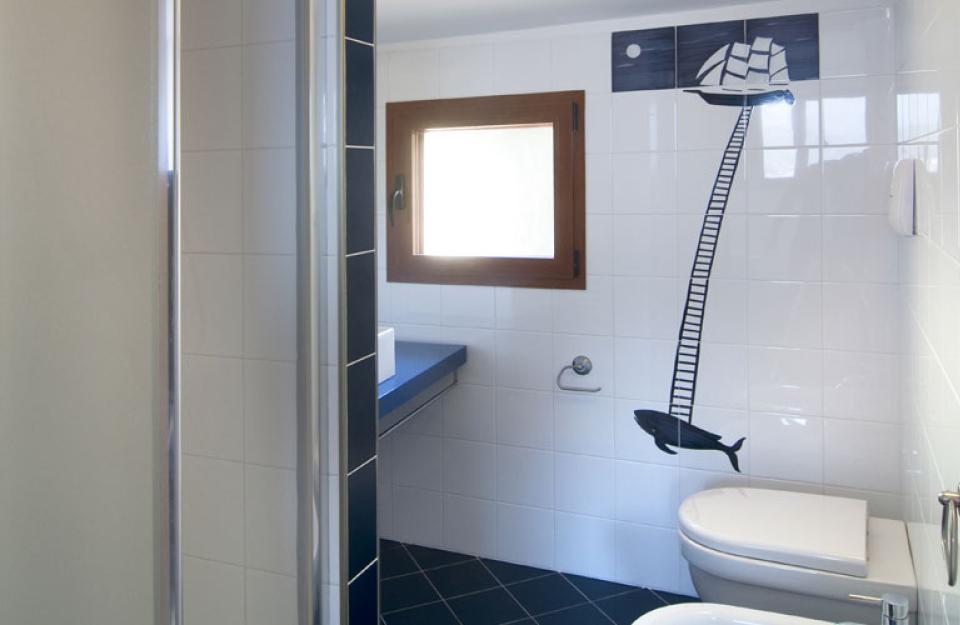 Bagno moderno con decorazioni murali di nave e balena, finestra e sanitari bianchi.