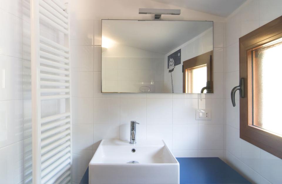 Bagno moderno con specchio, lavabo bianco, finestra e scaldasalviette.