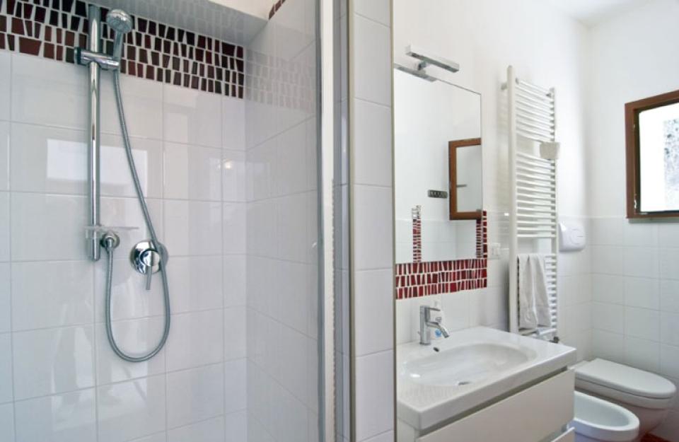 Bagno moderno con doccia, lavabo, specchio e finestra, decorato con piastrelle bianche e rosse.