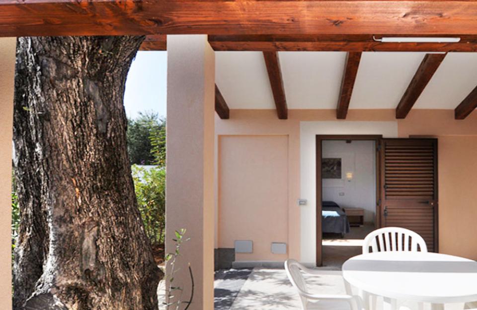 Terrazza con tavolo bianco, sedie, travi in legno e vista su giardino.