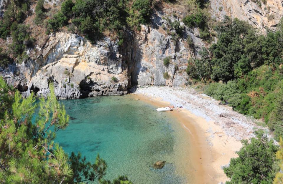 Spiaggia con barca, bagnanti e scogli, immersa in una baia tranquilla.