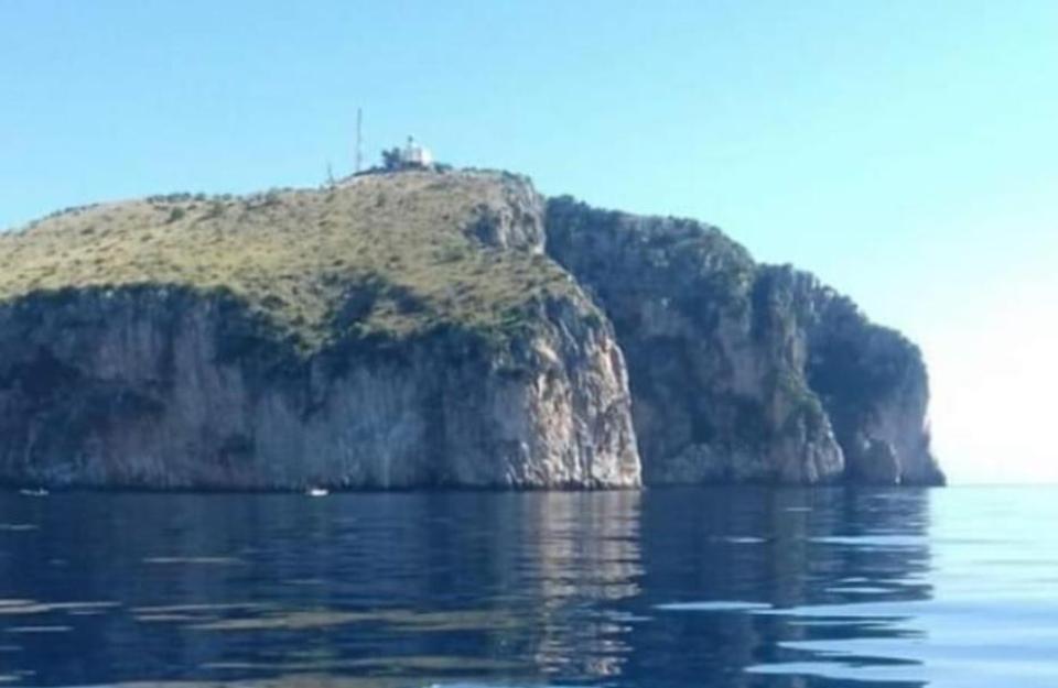 Isola rocciosa con faro, riflessa nel mare calmo sotto un cielo sereno.